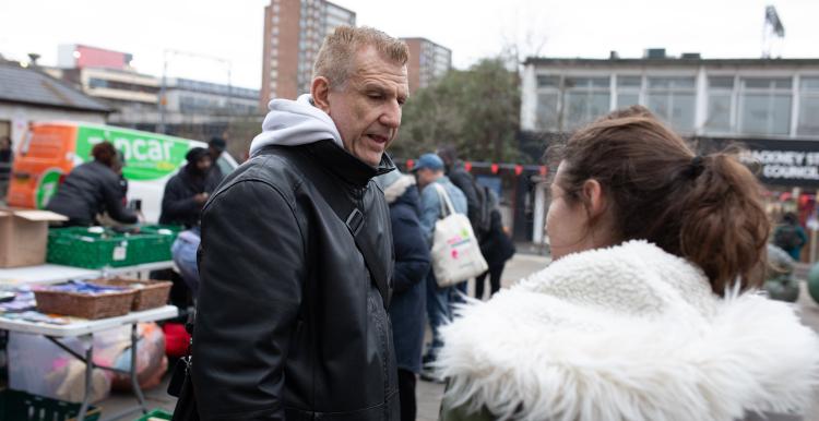Man an woman talk outside on street, wrapped up in winter coats.
