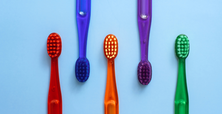 Five different coloured toothbrushes on a blue background.