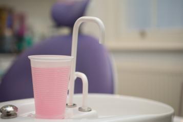 Cup of pink mouthwash on sink in dental practice