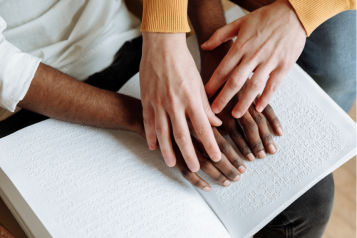Two pairs of hands tracing braille on a book.
