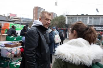 Man an woman talk outside on street, wrapped up in winter coats.