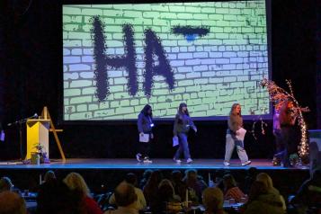 Young people deliver a presentation on a stage in front of a large crowd