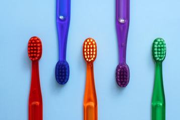 Five different coloured toothbrushes on a blue background.