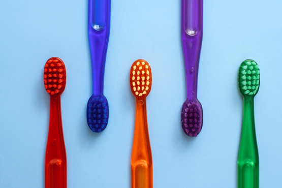 Five different coloured toothbrushes on a blue background.