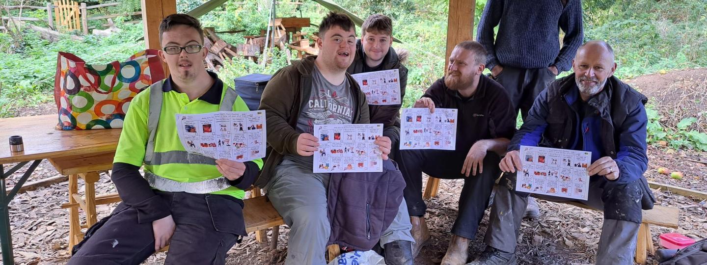A group of men sit outside on wooden benches and hold signs.