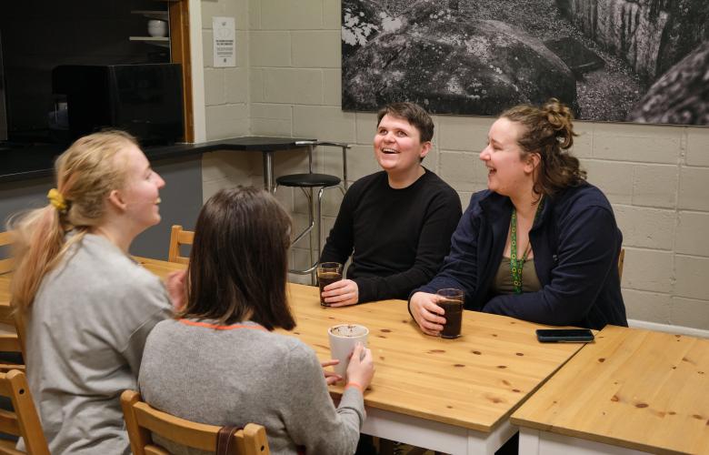 four women sit around a table and are laughing