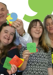 A group of people smile at the camera whole holding post-it notes with thumbs up drawn on them.