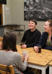 four women sit around a table and are laughing