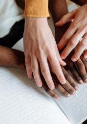Two pairs of hands tracing braille on a book.